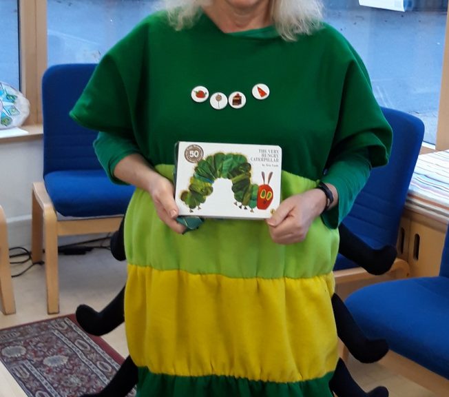 Woman wearing a caterpillar costume holding 'My Very Hungry Caterpillar'