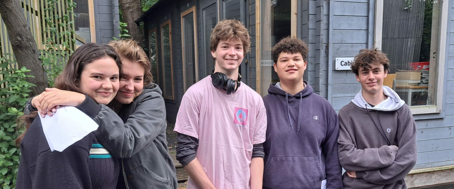 Five Sixth Form students from The King Alfred School shown smiling, with two holding their A level results certificates