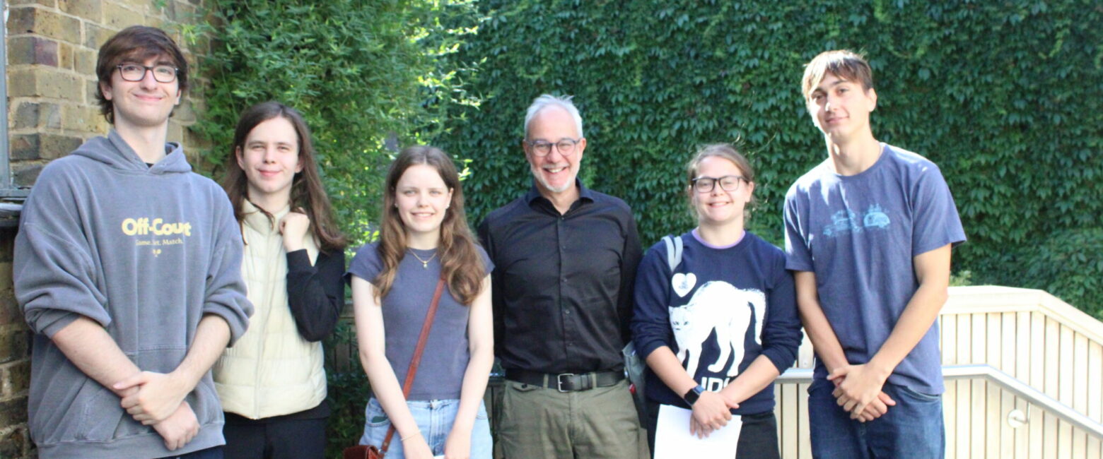 Robert Lobatto, a white male and Head Teacher at The King Alfred School, smiles with a group of five Sixth Form students in front of a school building on A level results day