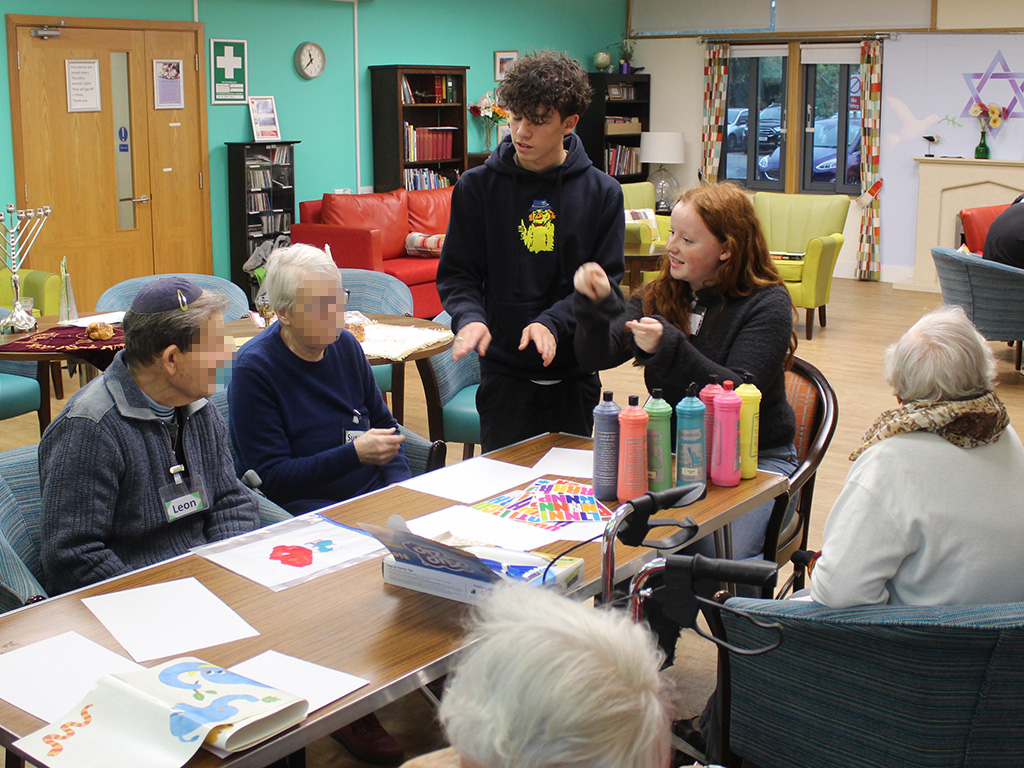 Sixth Form students from The King Alfred School and care home residents sit around a table with tubes of paint and paper