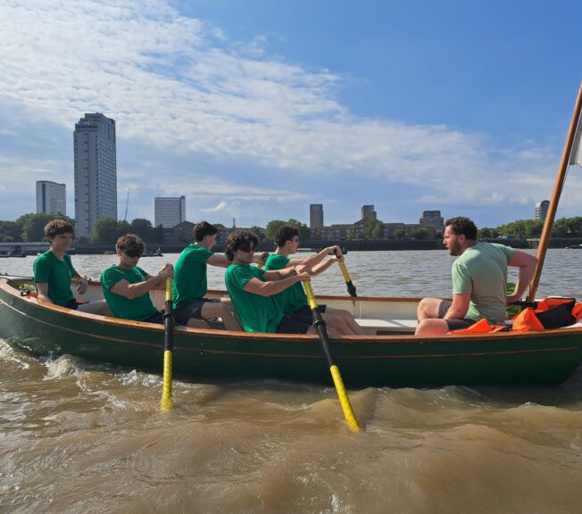 Side-shot of a rowing boat on the River Thames, with five students from The King Alfred School Sixth Form rowing and a teacher coxing