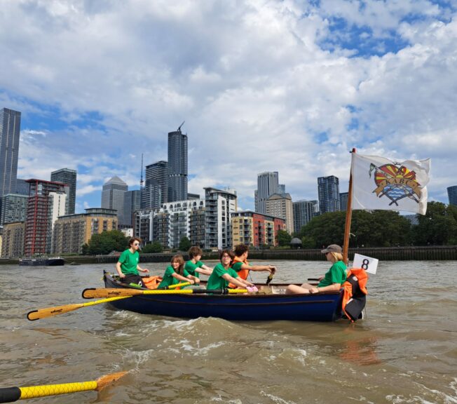 Students from The King Alfred School Sixth Form pictured rowing a boat along the Thames, with Canary Wharf in the backrground