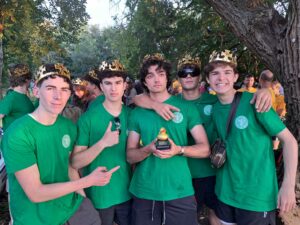 Five male students from The King Alfred School Sixth Form wear green school t-shirts and comedy crowns, with one holding a rubber duck trophy