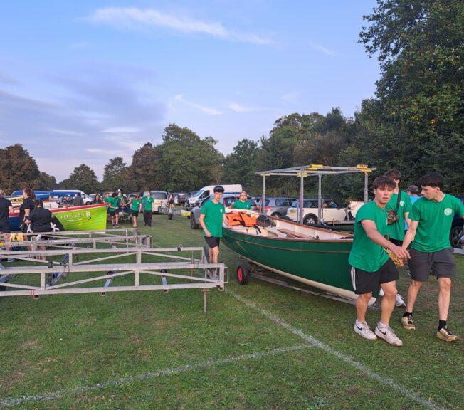 Students from The King Alfred School Sixth Form pull a rowing boat on wheels across grass