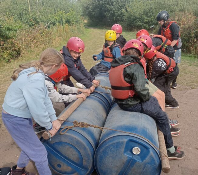 Students from The King Alfred School build a raft using blue barrels, rope and rods of wood