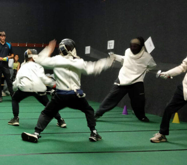 Students from The King Alfred School in a black fencing room lunge at one another using sabres