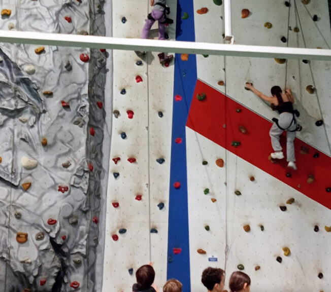 Students from The King Alfred School climb a white climbing wall using ropes