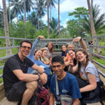 A group of students and staff members from The King Alfred School sit smiling in the back of an open-air truck with palm trees in the background