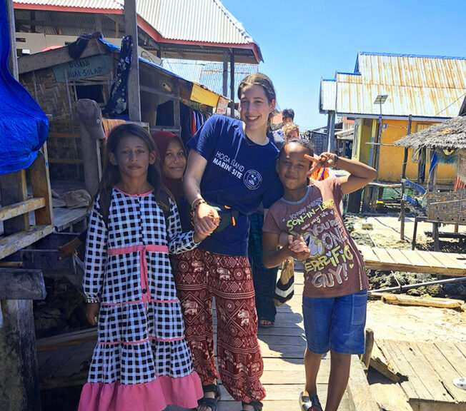 A student from The King Alfred School and local Indonesian children hold hands and smile