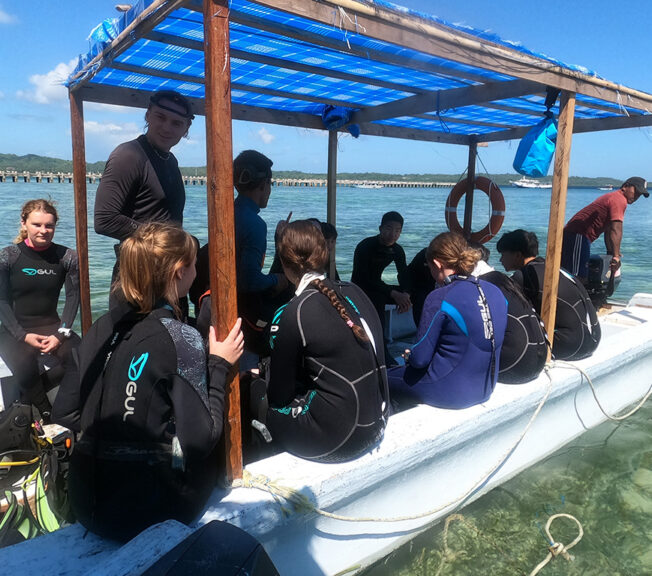 A group of students from The King Alfred School wearing wetsuits and sitting in a basic boat in the Indonesian sea