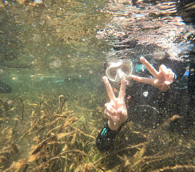 A student from The King Alfred School makes peace signs with their fingers underwater