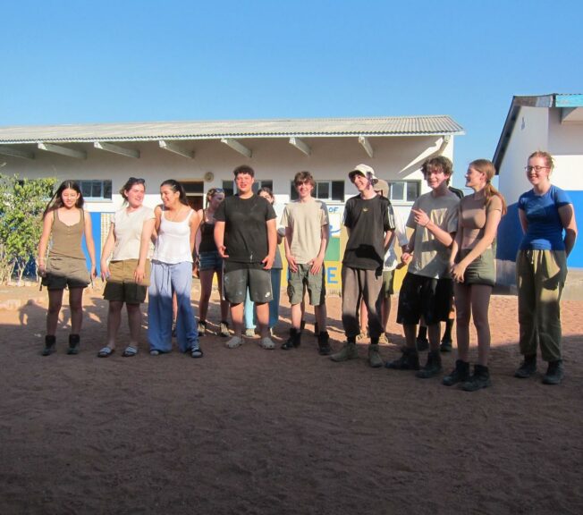 Students from The King Alfred School stand in a line in front of a Namibian school