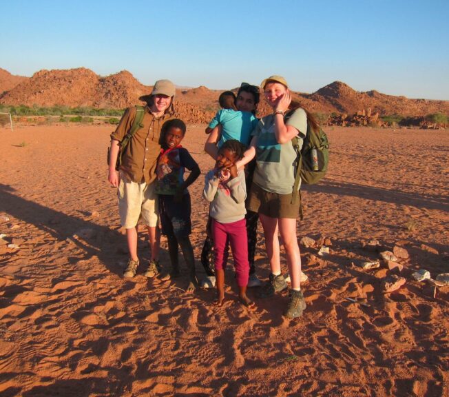 Two students from the King Alfred School pose with local children in the Namibia desert