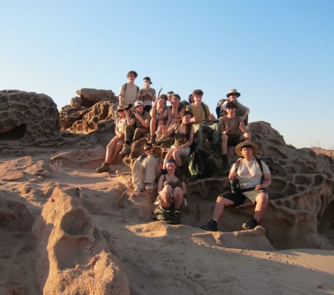 Students from The King Alfred School sit on a hillside in the Namibia desert