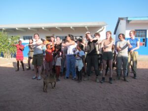 Students from The King Alfred School stand in a line outside, dancing with local children