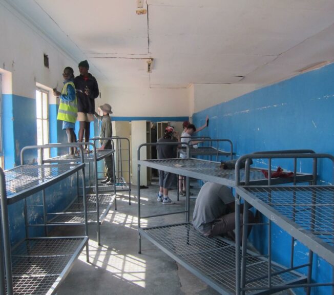 Students from The King Alfred School stand on ladders painting the walls of a school in Namibia