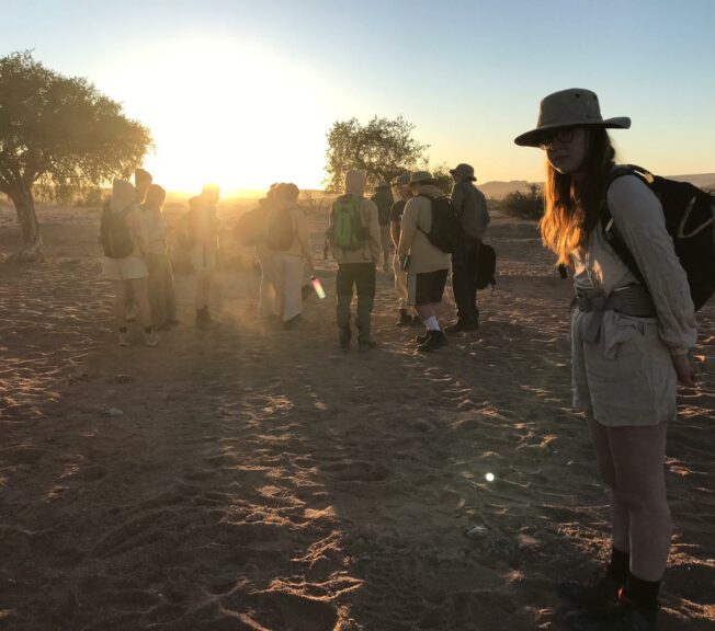 Students from The King Alfred School stand in the Namibia desert as the sun goes down over the horizon