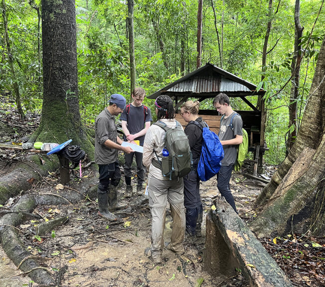 A group stand in the Indonesian rainforest looking at a map with a guide