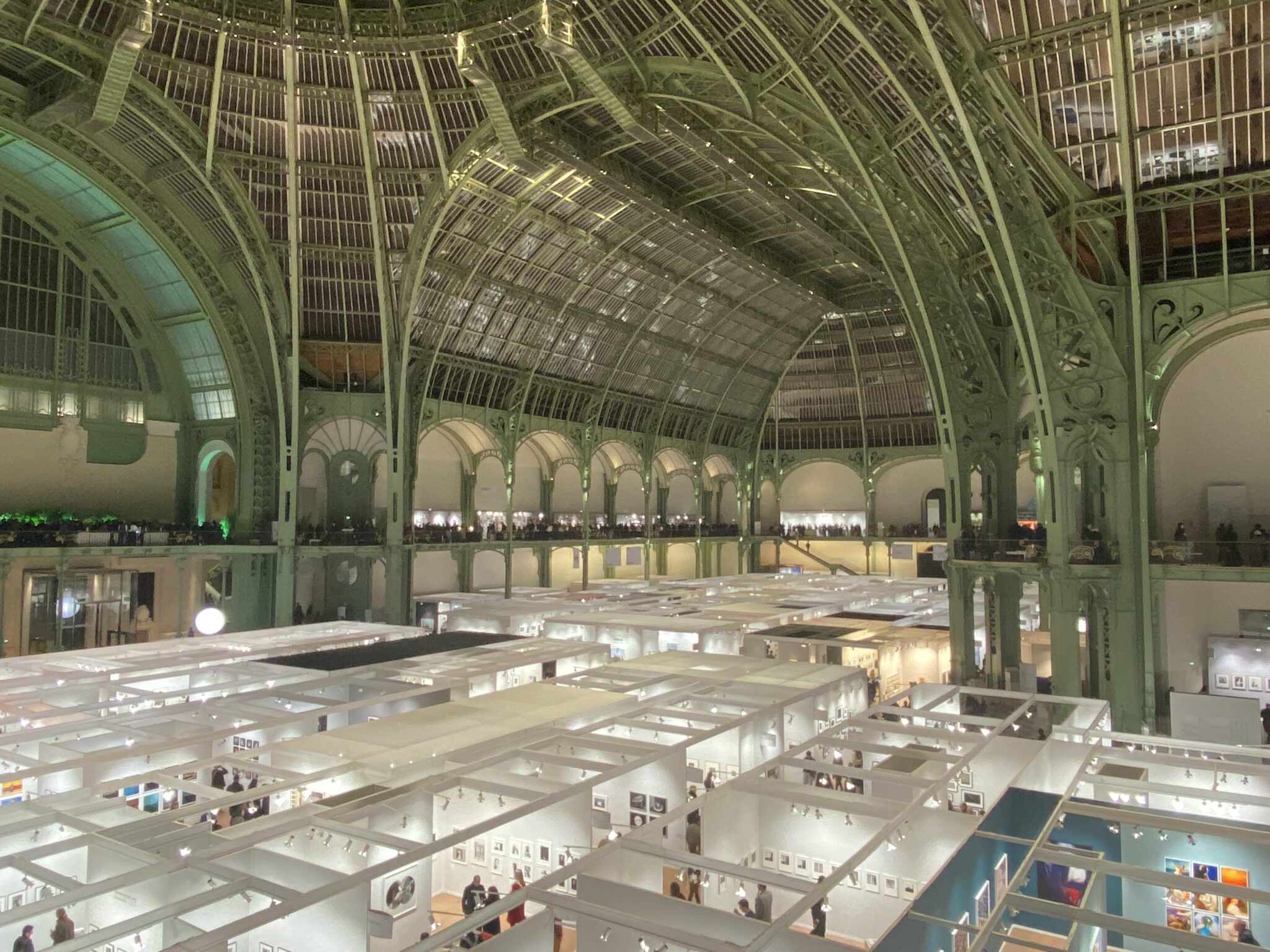 The Grand Palais in Paris set up for the Paris Photo photography fair. White booths can be seen set-up underneath the venue's distinctive green arches.