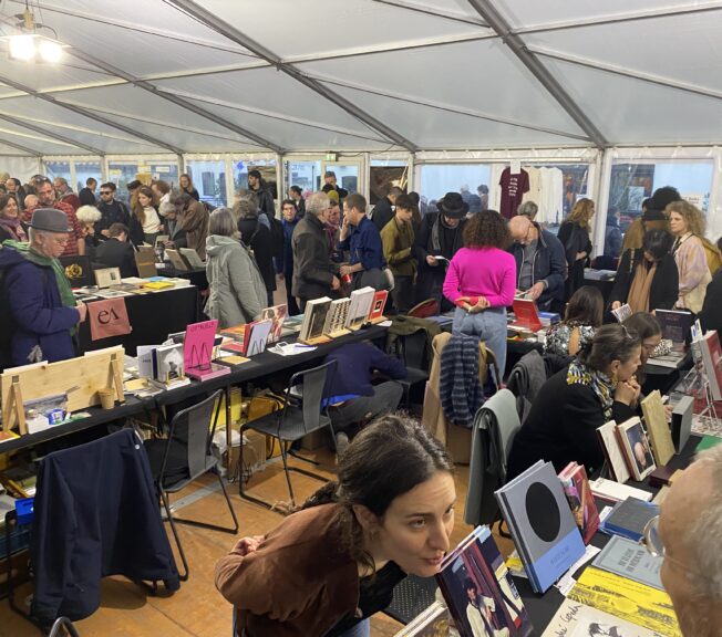 A packed room of people browsing tables of art books at Paris Photo