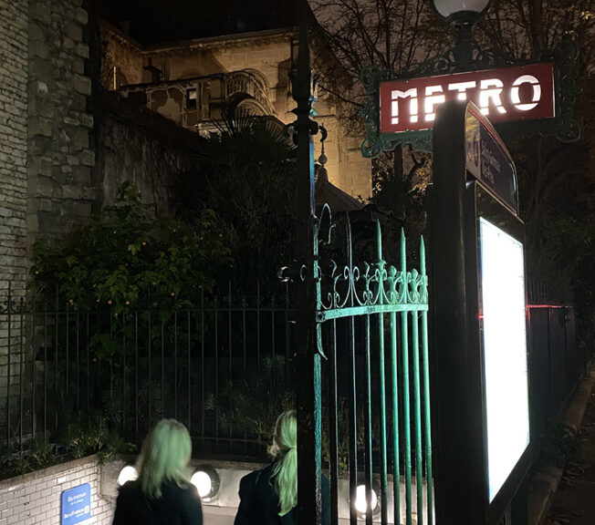 Two female Sixth Form students from The King Alfred School walk down the steps of a Paris Metro station at night