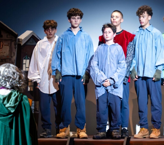 A group of boys on stage in The Ballard of Raggedy Alice, wearing baggy shirts