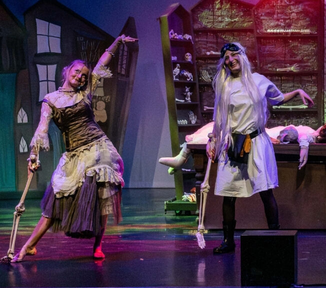 Two female actors dance with bone props on stage