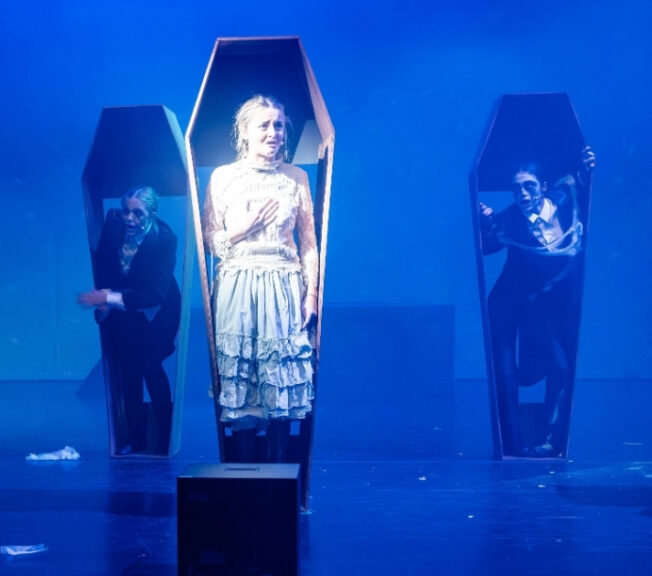 Actors perform inside coffins stood up on stage