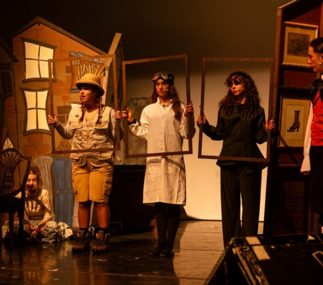 Three performers hold empty picture frames on stage