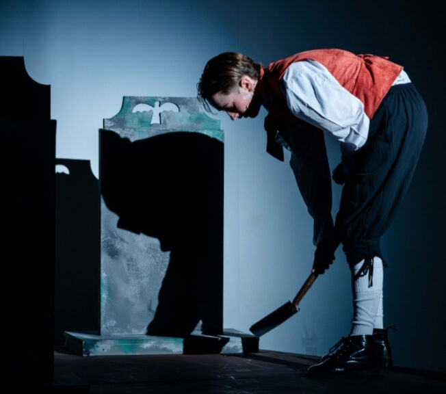 An actor is seen digging a grave on stage