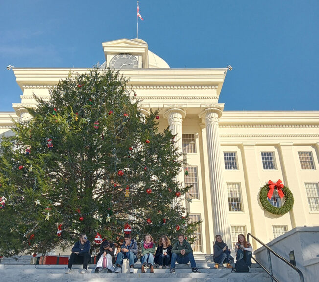 Students from The King Alfred School stand in front of a Christmas tree outside of the Greek Revival-style Alabama State Capital building