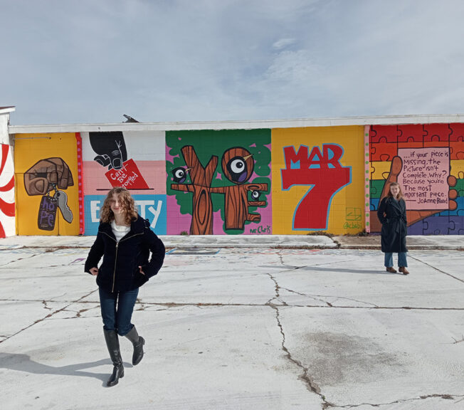 Two female students stand in front of colourful civil rights murals