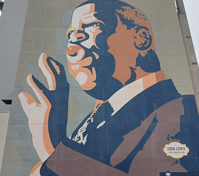 Students stand in front of a huge mural of Civil Rights activist John Lewis, which features the word 'HERO'