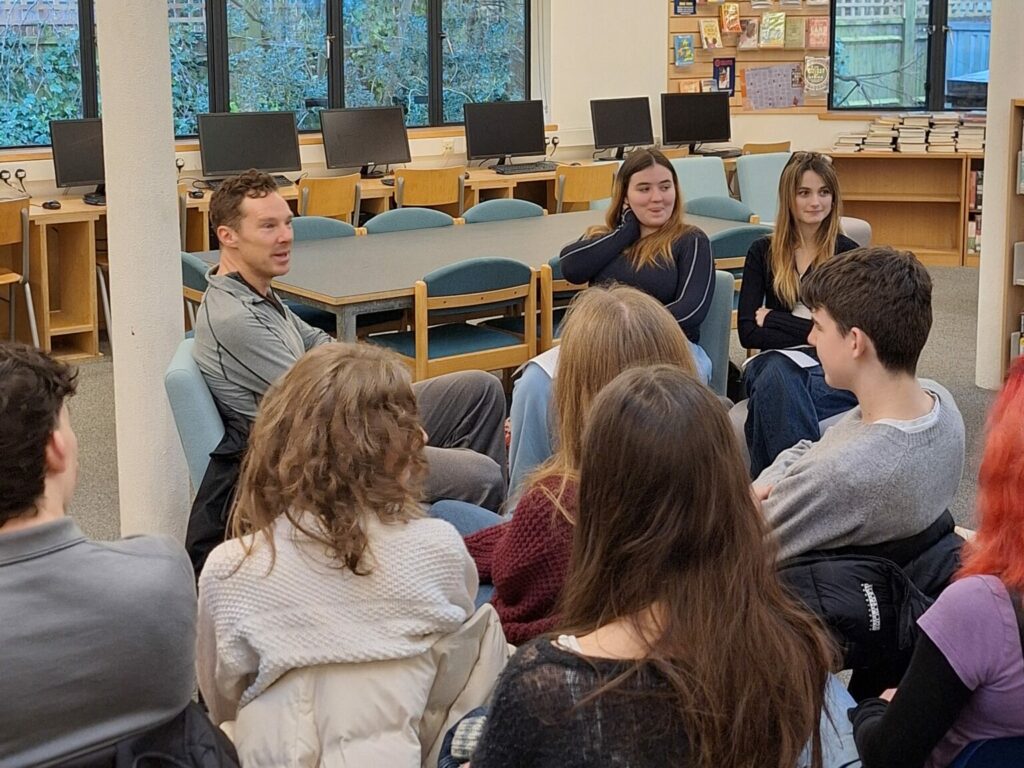 A white male addresses a brightly-lit room of students