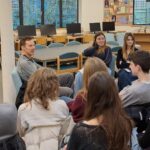 A white male addresses a brightly-lit room of students