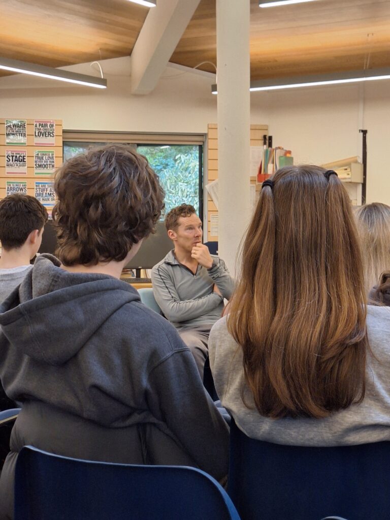 A white man is seen through a crowd of students, touching his chin in deep thought