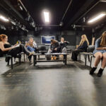 Six students from The King Alfred School North London sit on chairs around a low table as they perform a play in the rehearsal studio