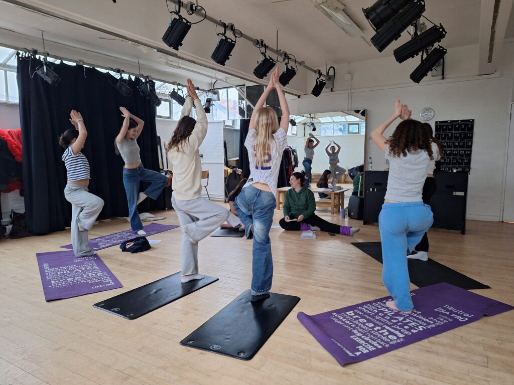 Female students perform tree pose on yoga mats in a bright and airy studio space