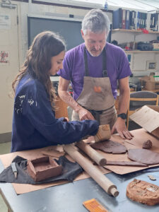 A teacher shows a Year 7 student how to roll out their relief sculpture in an Art lesson at The King Alfred School North London