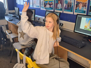 A student puts up their hand while working on the computer in the ICT lab at The King Alfred School North London